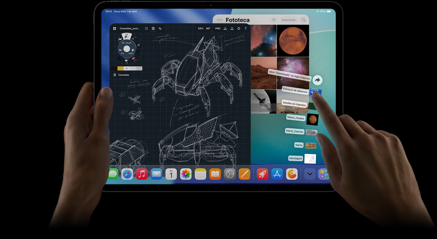Parte da frente do iPad Pro na horizontal. A mão direita gesticula sobre os arquivos na pasta Downloads, que estão espalhados em formato de leque. A tela mostra a interface do iPadOS 26 com a Fototeca e apps abertos, incluindo um app de edição de fotos com projetos detalhados de robôs, anotações manuscritas e várias etapas de design