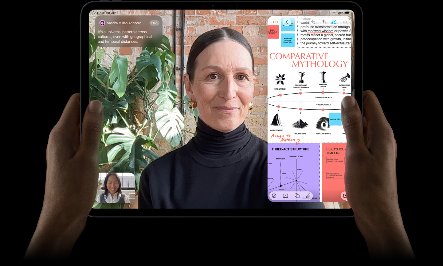 iPad Pro, front exterior, space black colour, left and right hands holding in landscape orientation, rounded corners, black display bezel, display showing a FaceTime conversation being live translated, and an educational app showing a presentation of 'Comparative Mythology' with text, diagrams and handwritten notes