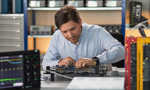 Greg a trabalhar num laboratório de engenharia de hardware, rodeado de equipamento de testagem de silício.