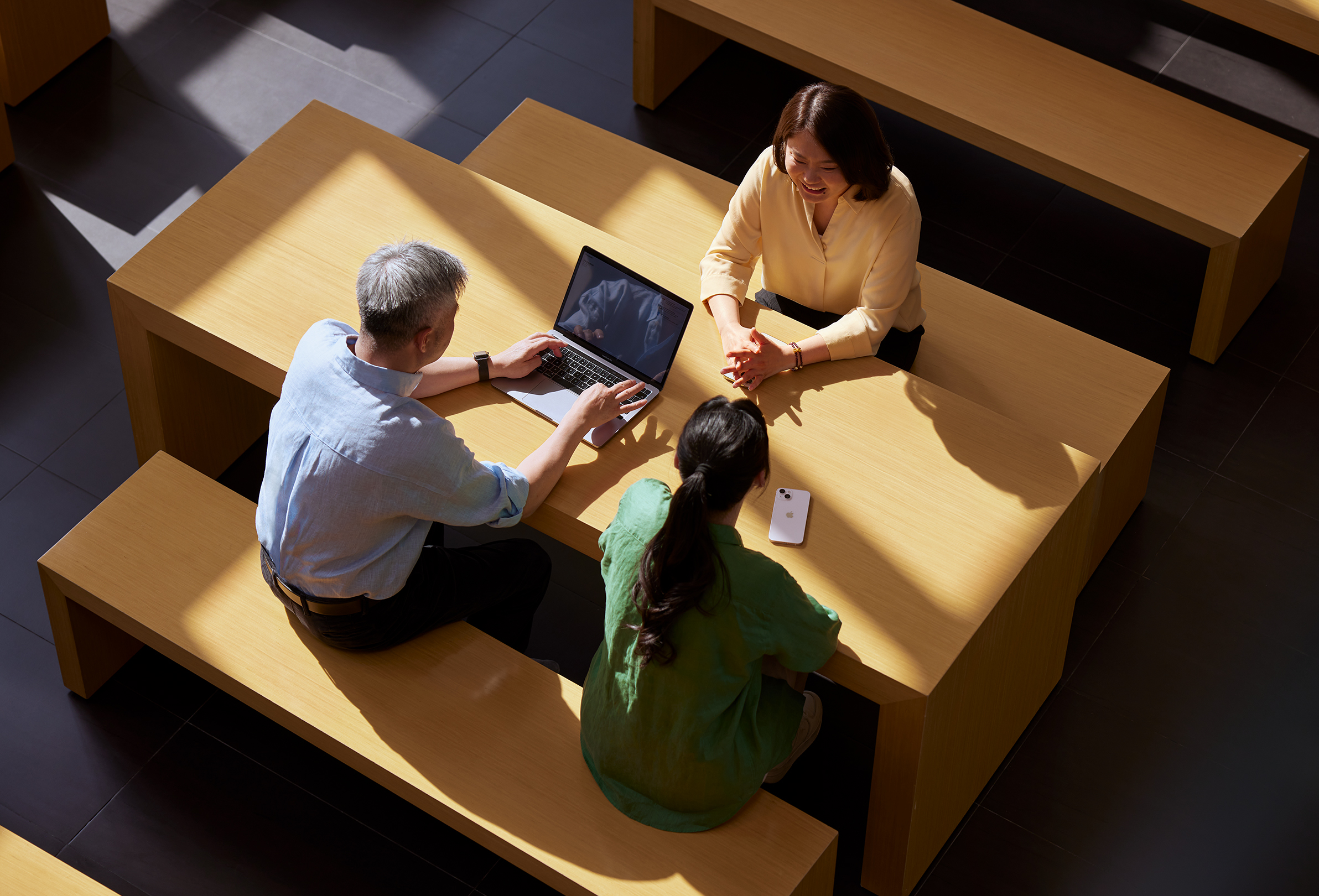 Tres empleados de Apple sentados en una mesa mientras uno de ellos trabaja en un MacBook.