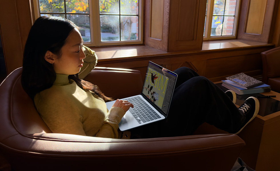 Seseorang sedang duduk di kursi sambil menggunakan MacBook Air