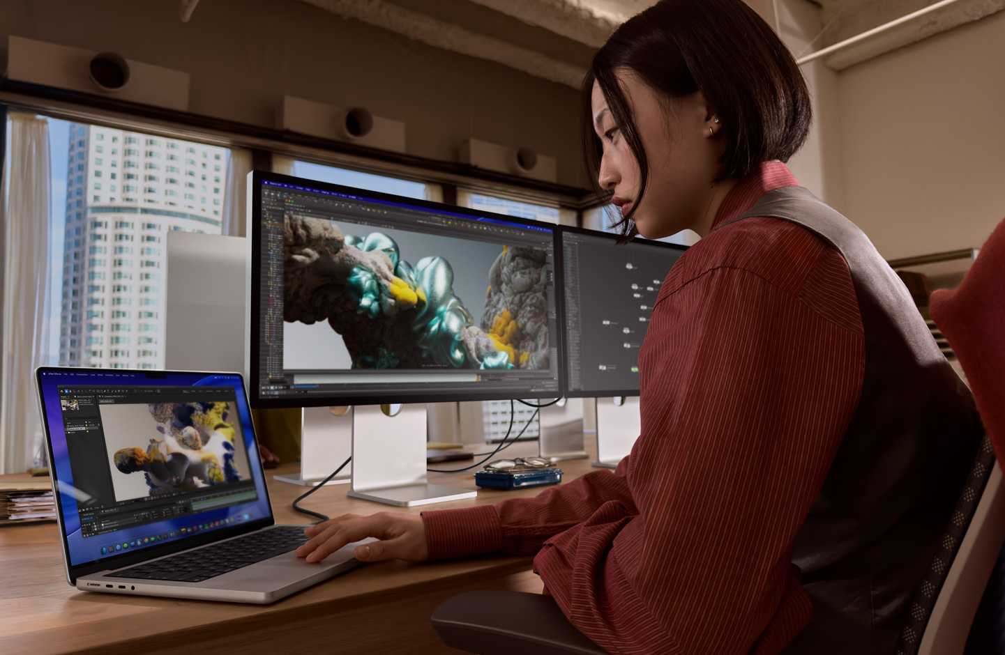 Bir ofis ortamında, Thunderbolt 5 bağlantı noktasıyla Studio Display XDR’a bağlı MacBook laptopta çalışan bir kişi