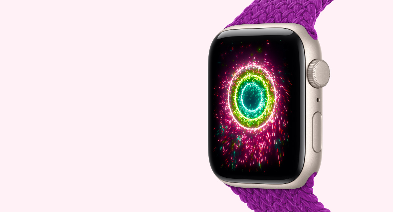 Apple Watch SE 3, starlight colour aluminium case connected to magenta colour Braided Solo Loop strap, screen shows Activity rings styled as sparklers, pink, lime green, light blue concentric rings