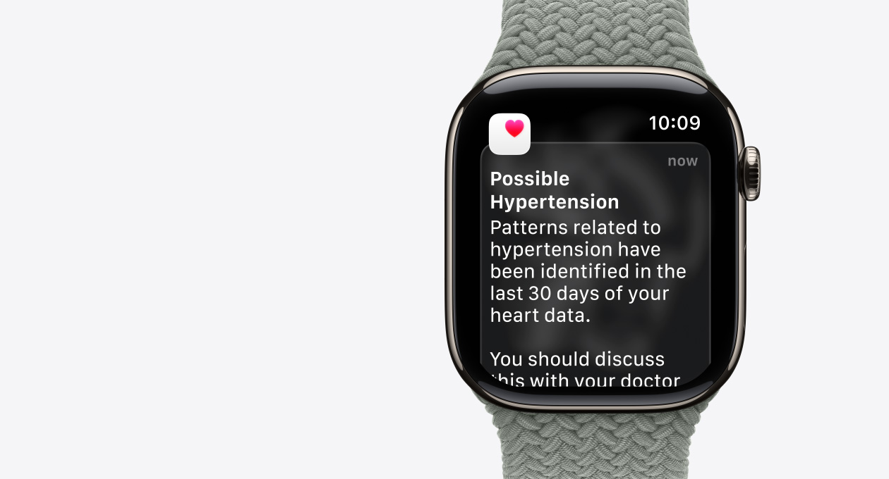 Apple Watch Series 11, натурален цвят, титанов корпус, възможно известяване за хипертония, розово сърце в бяла кутия, дясна външна част, Digital Crown, каишка, зелено-сива Braided Solo Loop