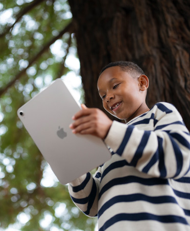 Un joven estudiante sonríe mientras usa un iPad al aire libre, se destaca la posibilidad de aprender en cualquier lugar