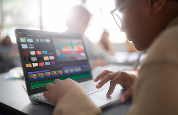 Una estudiante usa iMovie en el Mac para editar un proyecto de video, elige entre distintos fondos, lo que demuestra un aprendizaje práctico