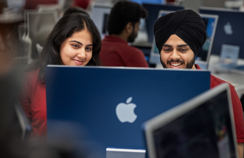 Hai sinh viên mỉm cười, cùng nhìn vào một màn hình iMac trong lớp học.