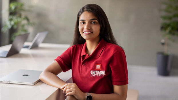 Nishtha Tandon ngồi tại bàn, bên cạnh là chiếc MacBook đã gập lại, cô mỉm cười nhìn vào camera.