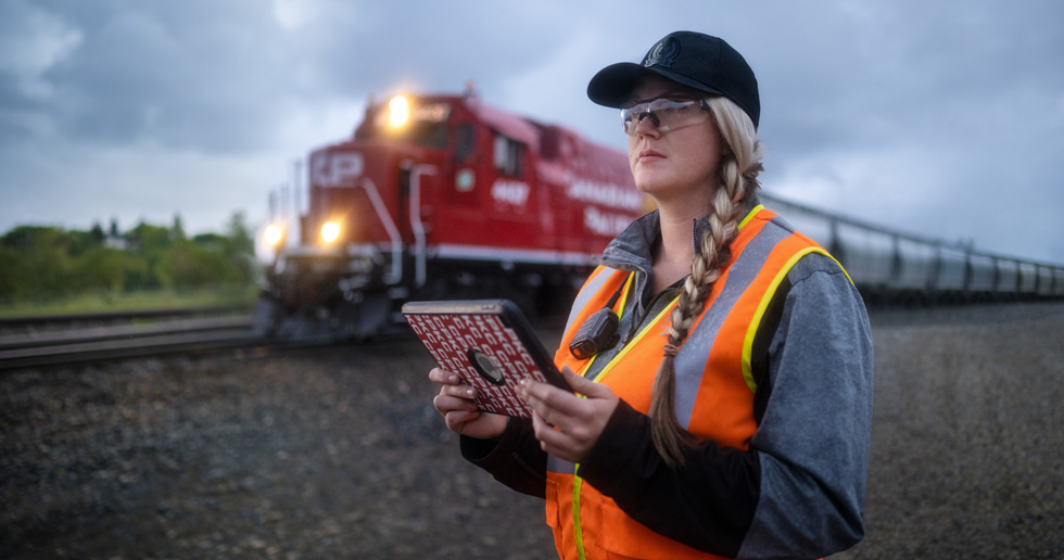 A railway worker holds an iPad and looks out at the tracks as a train passes by