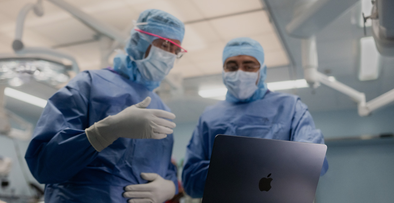To kirurger diskuterer noget på en MacBook Pro-skærm på operationsstuen.