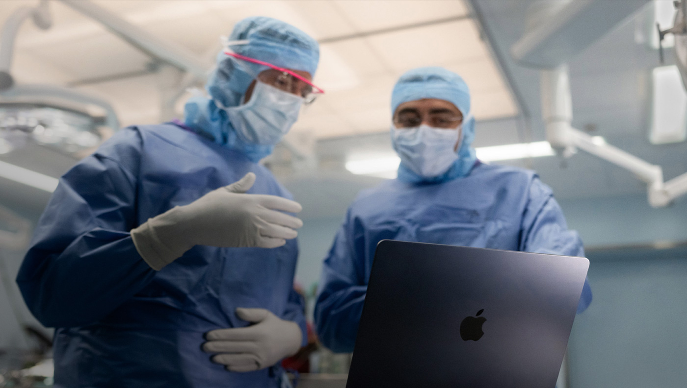 To kirurger diskuterer noget på en MacBook Pro-skærm på operationsstuen.