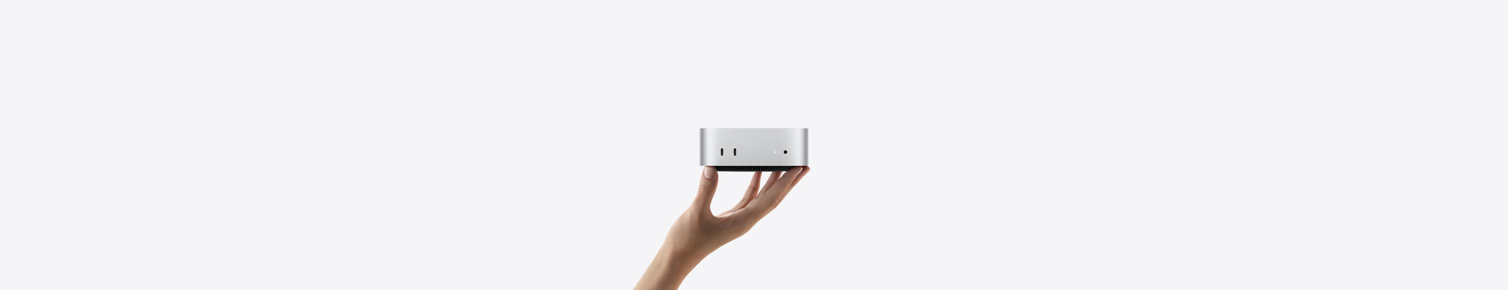 Vista frontal do Mac mini equilibrado na ponta dos dedos de uma mão esticada com a palma para cima, com as duas portas Thunderbolt à vista, luz indicadora de estado e saída para auscultadores, base afunilada, parte superior plana, moldura reta com arestas arredondadas, na cor prateado