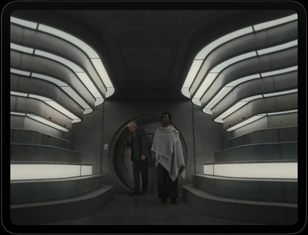 iPad Pro, front exterior, landscape orientation, space black colour, black display bezel, display showing futuristic spacecraft with detailed machinery, individual in spacesuit interacting with controls and equipment