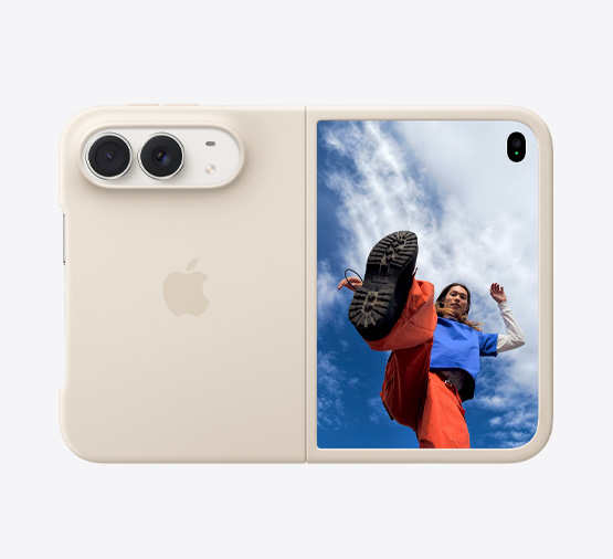 サンドのシリコーンケースが装着された、横向きのスターホワイトのiPhone Duo。横向きで完全に開いた状態。左上にDual Fusionカメラ。ケースが背面の外観と前面のディスプレイの外周を覆っている。右側にはアウターディスプレイが見えており、雲に覆われた青空の下に立つ人物の画像が表示されている