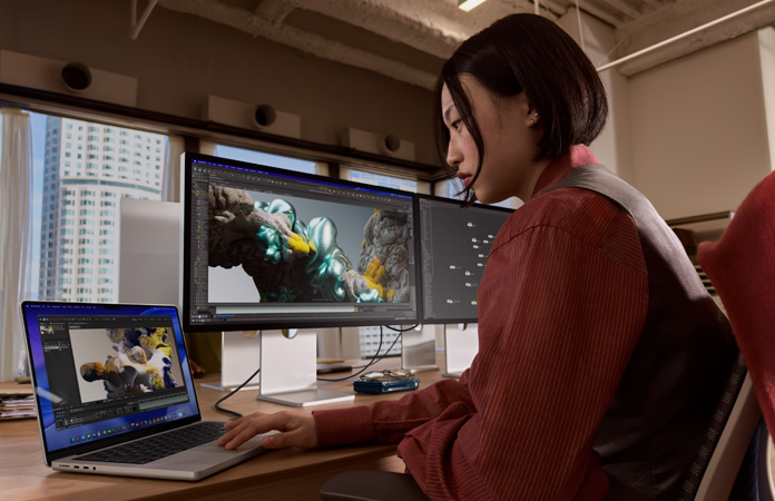 Una persona trabaja en una oficina con un MacBook Pro conectado a un monitor Studio Display XDR