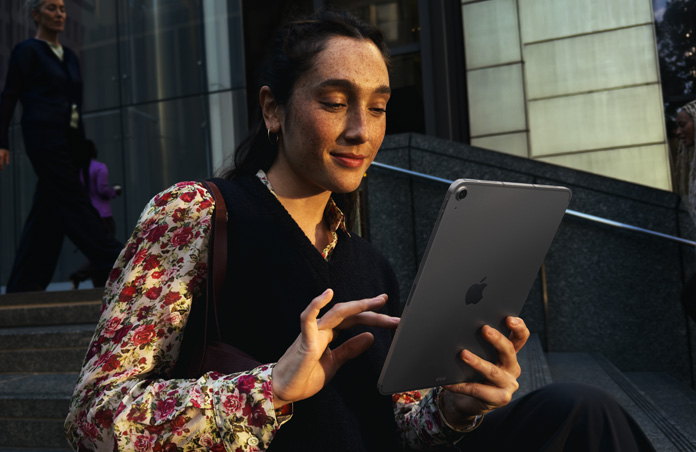 Person sitting on steps outside a large building using an iPad Air 11-inch in Space Grey, maintaining seamless Wi‑Fi connection across network transfers