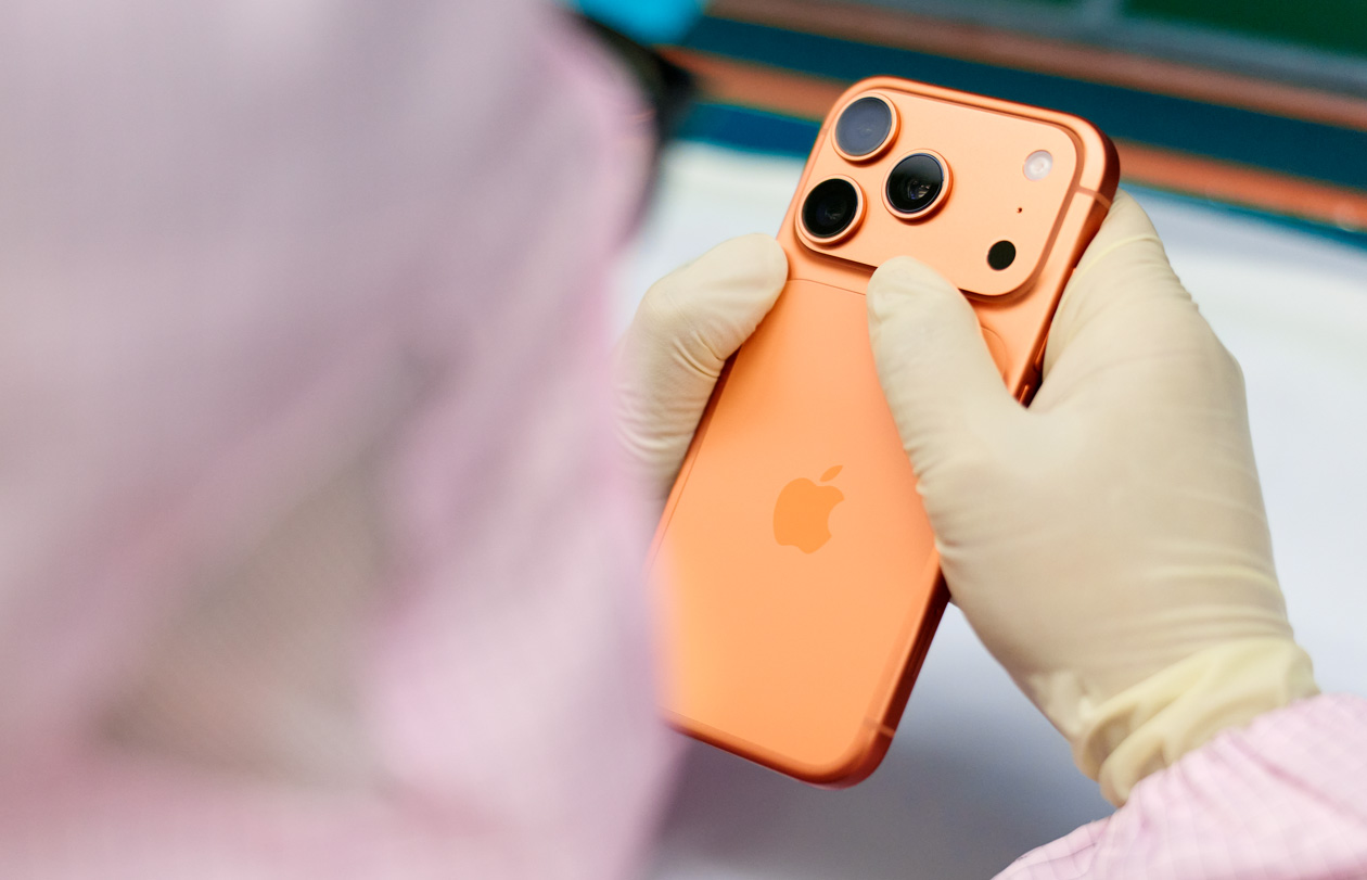 An employee in full-body work suit inspects an iPhone at a workstation