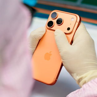 An employee in full-coverage work suit inspects an iPhone at a workstation