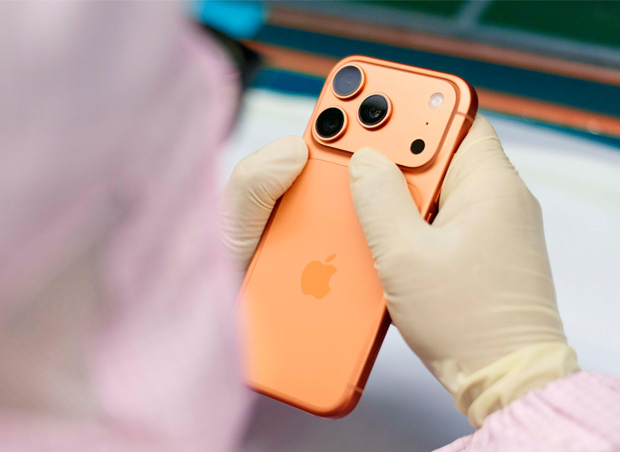 An employee in full-coverage work suit inspects an iPhone at a workstation