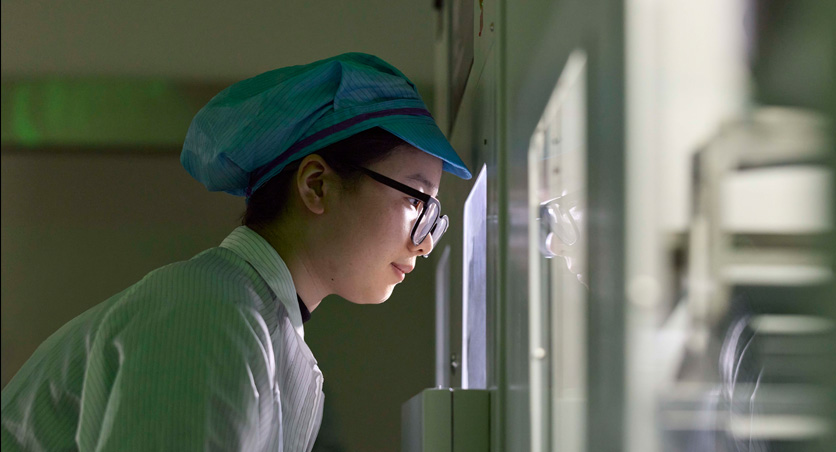 An employee in full-coverage work suit and eyewear observes Apple Watch assembly